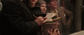 Movie still from “Cinderella Man” (2005), directed by Ron Howard – An older person writing on a piece of paper in front of a crowd; Close Up shot, Over the shoulder angle