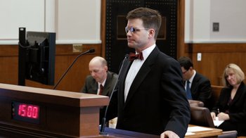 Movie still from “Citizenfour” (2014), directed by Laura Poitras – A man in a suit and bow tie standing in front of a microphone; Close Up shot, Over the shoulder angle