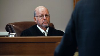Movie still from “Citizenfour” (2014), directed by Laura Poitras – An older man wearing a robe in a court room; Close Up shot, Over the shoulder angle