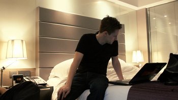 Movie still from “Citizenfour” (2014), directed by Laura Poitras – A man sitting on top of a bed with a computer; Medium shot, High angle
