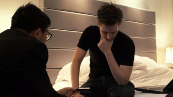 Movie still from “Citizenfour” (2014), directed by Laura Poitras – A man sitting on a bed with another man holding a phone; Medium shot, High angle