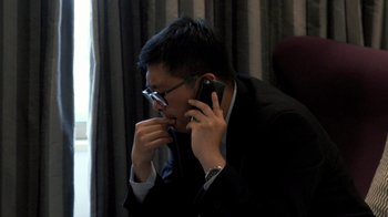 Movie still from “Citizenfour” (2014), directed by Laura Poitras – A man wearing a suit and glasses talking on a cell phone; Close Up shot, Low angle