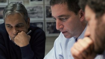 Movie still from “Citizenfour” (2014), directed by Laura Poitras – Two men sitting at a table with pens in their hands; Close Up shot, Over the shoulder angle