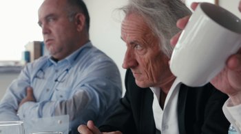 Movie still from “Citizenfour” (2014), directed by Laura Poitras – Two men sitting at a table and one of them is holding a phone; Close Up shot, Over the shoulder angle