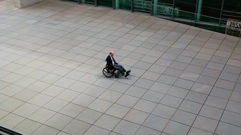 Movie still from “Citizenfour” (2014), directed by Laura Poitras – A man sitting in a wheel chair on a tiled floor; Extreme Wide shot, High angle