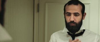 Movie still from “City of Ghosts” (2017), directed by Matthew Heineman – A man with a beard wearing a white shirt and a bow tie; Close Up shot, Low angle