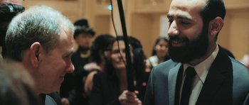 Movie still from “City of Ghosts” (2017), directed by Matthew Heineman – A man with a long beard is holding a microphone; Close Up shot, Over the shoulder angle