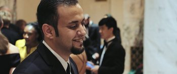 Movie still from “City of Ghosts” (2017), directed by Matthew Heineman – A man in a suit and tie smiling at the camera; Close Up shot, Low angle