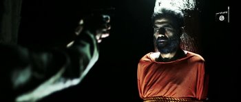 Movie still from “City of Ghosts” (2017), directed by Matthew Heineman – A man with a beard is standing in front of another man with a gun; Close Up shot, Over the shoulder angle