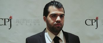 Movie still from “City of Ghosts” (2017), directed by Matthew Heineman – A man wearing a suit and tie standing in front of a white wall; Close Up shot, Low angle