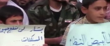 Movie still from “City of Ghosts” (2017), directed by Matthew Heineman – A man in a camouflage jacket holding a sign; Close Up shot, High angle