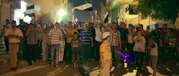 Movie still from “City of Ghosts” (2017), directed by Matthew Heineman – A group of people standing on a street at night; Wide shot, High angle
