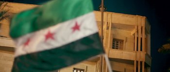 Movie still from “City of Ghosts” (2017), directed by Matthew Heineman – A syrian flag in front of a building; Medium shot, Low angle