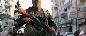 Movie still from “City of Ghosts” (2017), directed by Matthew Heineman – A man holding a gun in his hand while standing in the street; Medium shot, Low angle