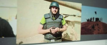 Movie still from “City of Ghosts” (2017), directed by Matthew Heineman – A man in a green vest holding a gun; Close Up shot, High angle