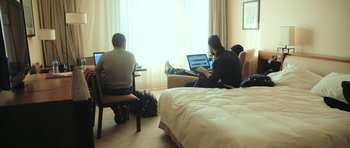 Movie still from “City of Ghosts” (2017), directed by Matthew Heineman – Two people sitting in a hotel room on their laptops; Wide shot, High angle