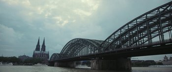 Movie still from “City of Ghosts” (2017), directed by Matthew Heineman – A large bridge over a body of water under a cloudy sky; Extreme Wide shot, Low angle