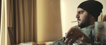Movie still from “City of Ghosts” (2017), directed by Matthew Heineman – A man sitting at a table with a cigarette in his hand; Close Up shot, Low angle