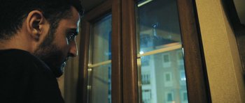 Movie still from “City of Ghosts” (2017), directed by Matthew Heineman – A man standing in front of a large window at night; Close Up shot, Low angle