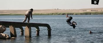 Movie still from “City of Ghosts” (2017), directed by Matthew Heineman – A man jumping in the air over a body of water; Extreme Wide shot, Low angle