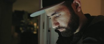 Movie still from “City of Ghosts” (2017), directed by Matthew Heineman – A man with a beard wearing a hat looking down; Close Up shot, Low angle