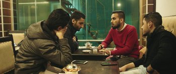 Movie still from “City of Ghosts” (2017), directed by Matthew Heineman – A group of men sitting at a table talking to each other; Medium shot, Over the shoulder angle