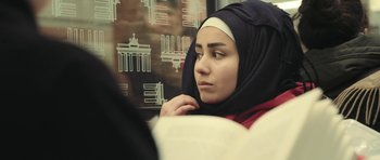 Movie still from “City of Ghosts” (2017), directed by Matthew Heineman – A young woman wearing a headscarf is sitting in front of a window; Close Up shot, Over the shoulder angle