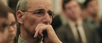 Movie still from “City of Ghosts” (2017), directed by Matthew Heineman – An older man with glasses is sitting in front of another man with his hand under his chin; Extreme Close Up shot, Low angle