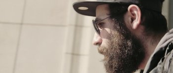 Movie still from “City of Ghosts” (2017), directed by Matthew Heineman – A person with a beard wearing glasses; Close Up shot, Low angle
