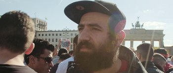 Movie still from “City of Ghosts” (2017), directed by Matthew Heineman – A man with a long beard wearing a black hat; Close Up shot, Low angle