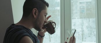 Movie still from “City of Ghosts” (2017), directed by Matthew Heineman – A man drinking a cup of coffee while looking at a tablet; Close Up shot, Low angle