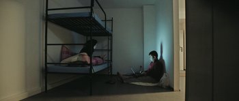 Movie still from “City of Ghosts” (2017), directed by Matthew Heineman – A man and a woman sitting on the floor in front of a bunk bed; Wide shot, High angle