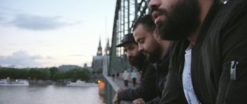 Movie still from “City of Ghosts” (2017), directed by Matthew Heineman – A group of men standing next to each other on top of a bridge; Close Up shot, Over the shoulder angle