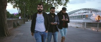 Movie still from “City of Ghosts” (2017), directed by Matthew Heineman – A group of men walking down a sidewalk with their cellphones; Medium shot, Low angle