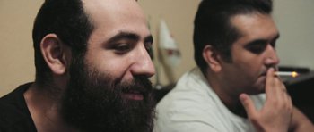 Movie still from “City of Ghosts” (2017), directed by Matthew Heineman – A man with a long beard is looking at the camera; Close Up shot, Over the shoulder angle