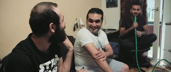 Movie still from “City of Ghosts” (2017), directed by Matthew Heineman – Two men sitting on a couch talking to each other; Medium shot, Over the shoulder angle