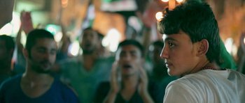 Movie still from “City of Ghosts” (2017), directed by Matthew Heineman – A group of young men standing next to each other on a city street; Close Up shot, Over the shoulder angle