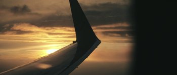 Movie still from “City of Ghosts” (2017), directed by Matthew Heineman – The wing of an airplane flying in the sky at sunset; Extreme Wide shot, Low angle