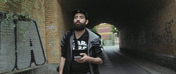 Movie still from “City of Ghosts” (2017), directed by Matthew Heineman – A man with a beard holding a cell phone in his hand; Medium shot, Low angle