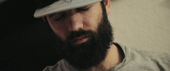 Movie still from “City of Ghosts” (2017), directed by Matthew Heineman – A man with a beard wearing a white hat; Close Up shot, Low angle
