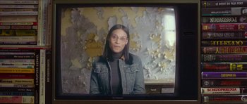 Movie still from “Climax” (2018), directed by Gaspar Noé – A woman wearing glasses and a jean jacket is sitting in front of a television screen; Close Up shot, Over the shoulder angle
