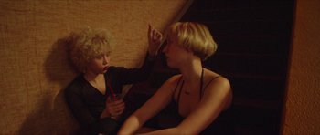 Movie still from “Climax” (2018), directed by Gaspar Noé – Two women sitting on a couch one of which is holding a pair of scissors; Medium shot, High angle