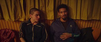 Movie still from “Climax” (2018), directed by Gaspar Noé – Two young men sitting on a bench in a room; Medium shot, Over the shoulder angle