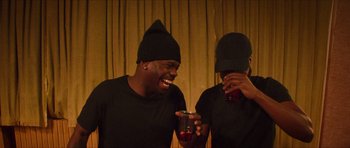 Movie still from “Climax” (2018), directed by Gaspar Noé – Two men in black shirts are laughing and holding drinks; Medium shot, High angle