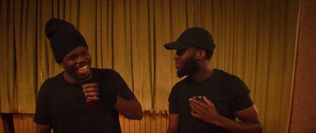 Movie still from “Climax” (2018), directed by Gaspar Noé – Two men in black shirts and a black hat are holding drinks; Medium shot, Low angle