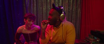 Movie still from “Climax” (2018), directed by Gaspar Noé – A man wearing headphones and eating something while sitting next to a woman; Medium shot, Over the shoulder angle