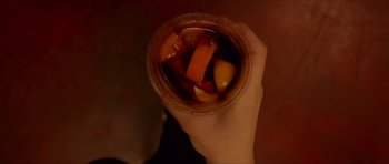 Movie still from “Climax” (2018), directed by Gaspar Noé – A person holding a cup of fruit on top of a wooden table; Extreme Close Up shot, Overhead angle