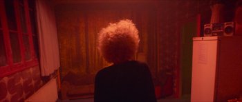 Movie still from “Climax” (2018), directed by Gaspar Noé – A person with a white afro is sitting in front of a red curtain; Medium shot, Over the shoulder angle
