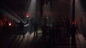 Movie still from “Cobra” (1986), directed by George P. Cosmatos – A group of men holding hammers in a dark room; Wide shot, High angle