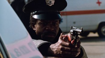 Movie still from “Cobra” (1986), directed by George P. Cosmatos – A police officer is holding a gun in his hand; Close Up shot, Low angle